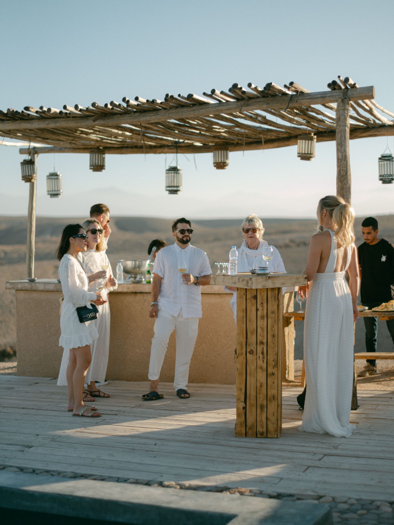 Guests in white gathering at an open-air pergola bar in the Agafay desert