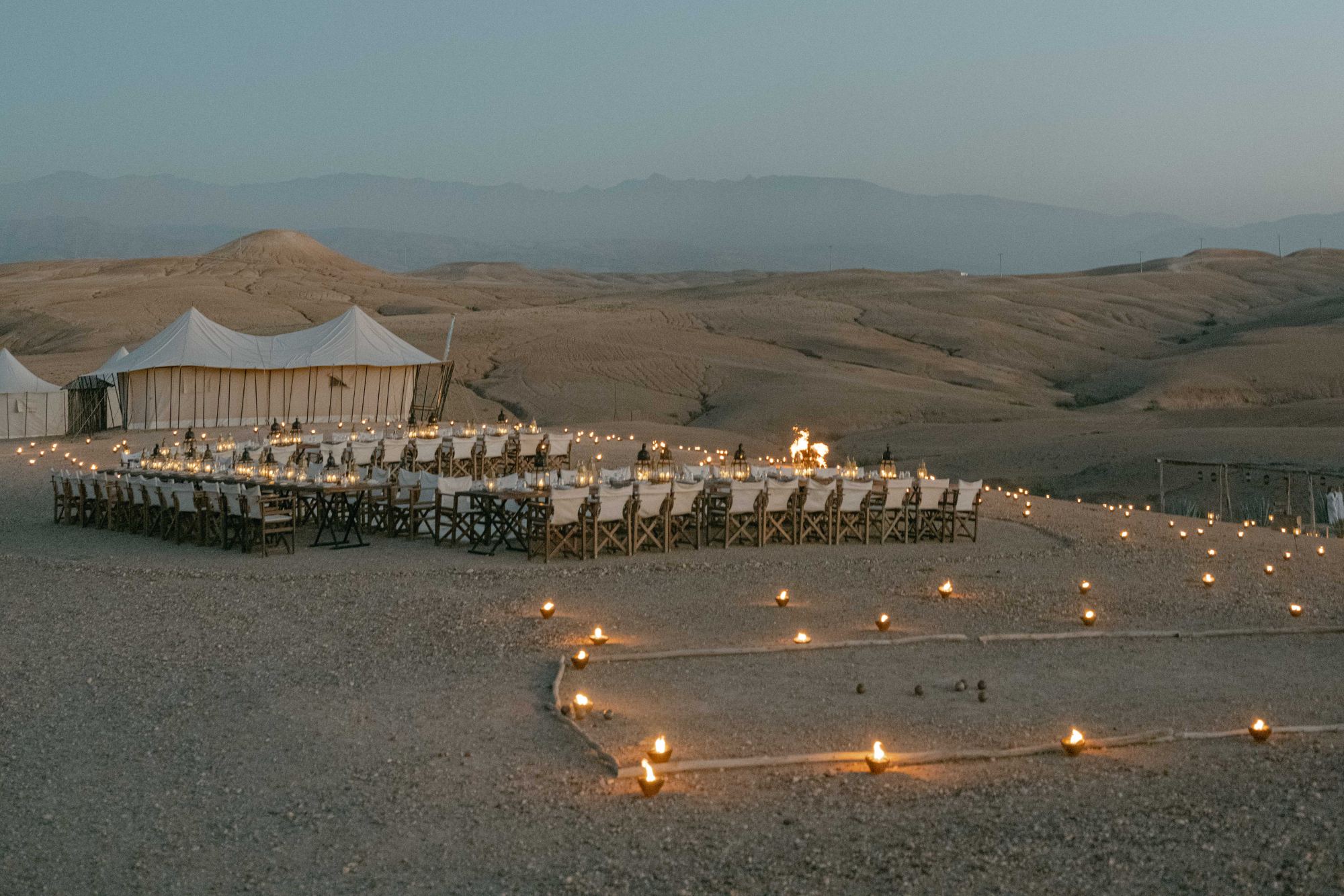 Candlelit dinner tables and white tents at dusk in the Agafay desert
