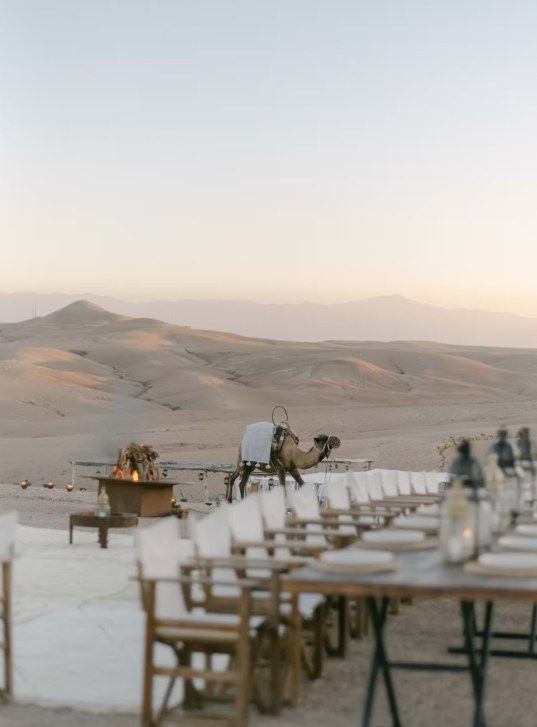 Dinner tables, fire bowl and camel at sunset in the Agafay desert