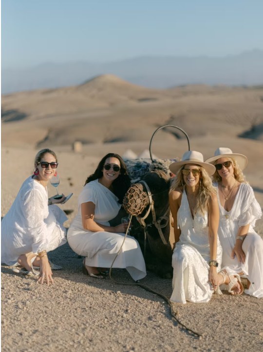 Agafay desert friends camel photo Friends in white posing with a camel during a desert celebration in Agafay