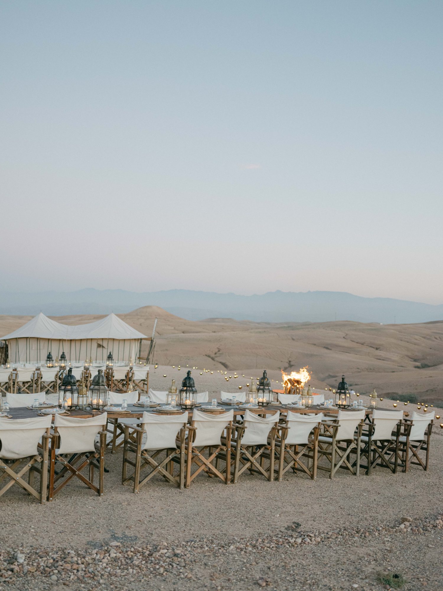 Long dinner table with lanterns in front of a white tent, Agafay desert